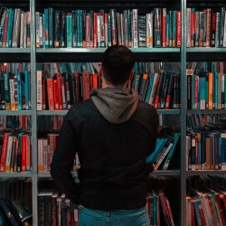 Man wearing black and grey jacket in front of book shelf.